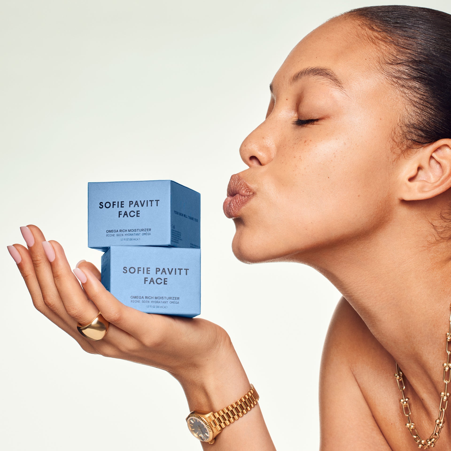 Woman holding and kissing a blue box of Sofie Pavitt Face skincare products on a light background