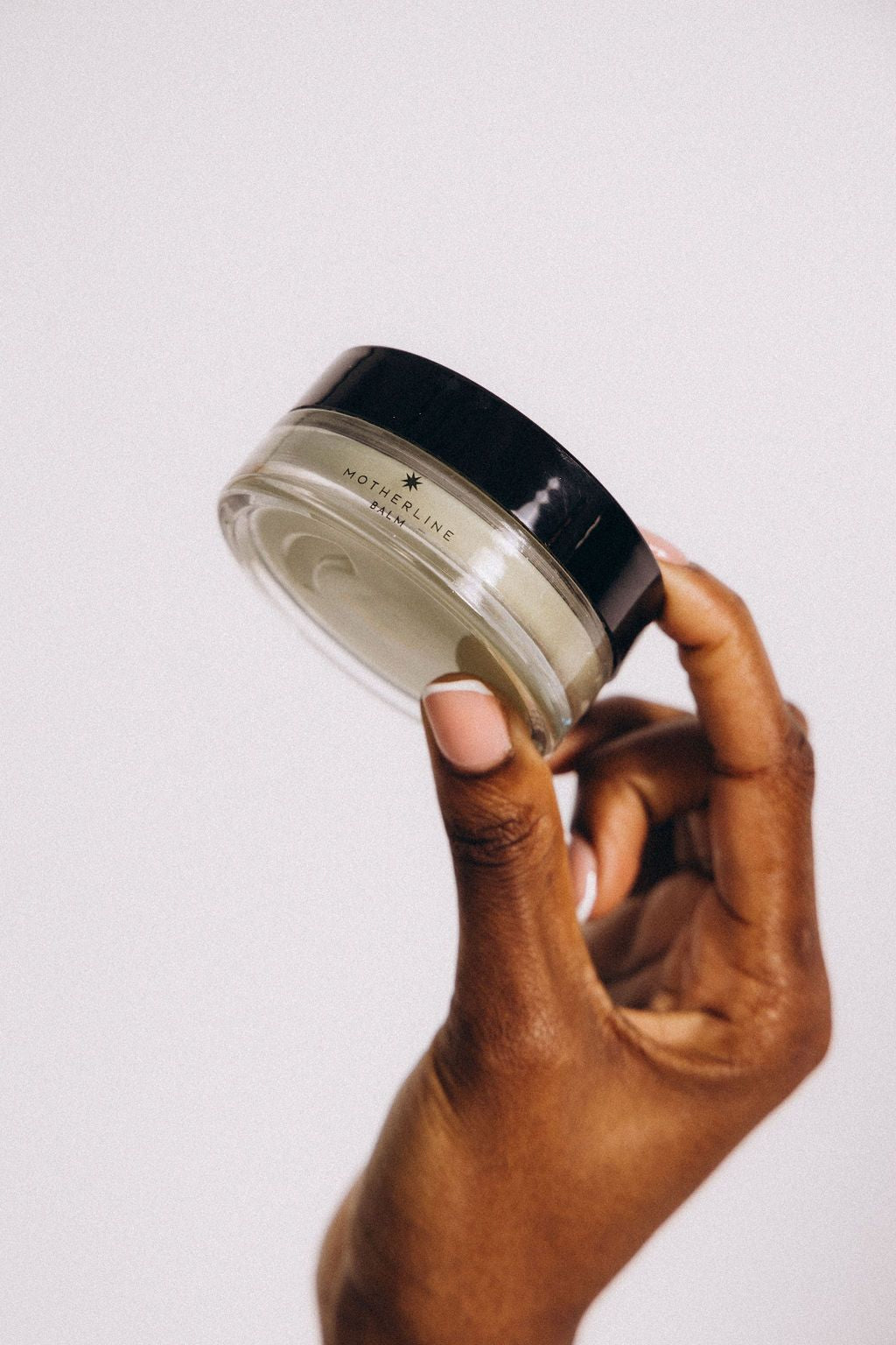 Motherline Balm in a small glass jar on a warm earthy background