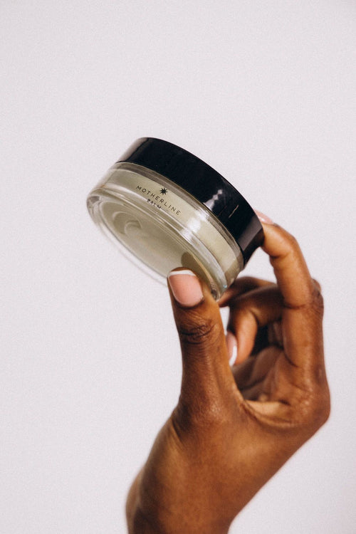 Motherline Balm in a small glass jar on a warm earthy background